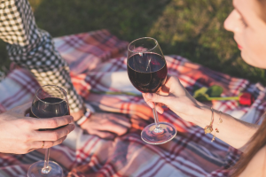Two people enjoying a glass of red wine on a picnic blanket