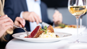 Diners eating a steak and vegetables with a glass of wine