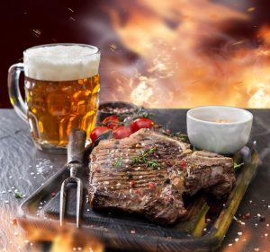 A steak on a grill next to a beer