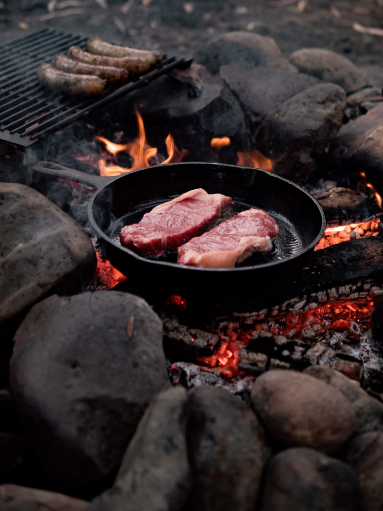Two steaks cooked over a fire and sausages grilling
