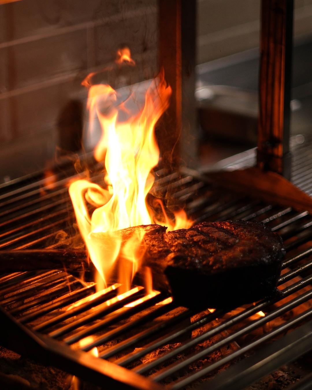 A steak being flame grilled on a grill at a steakhouse