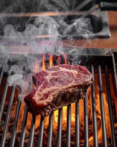 A steak cooking on a fire flamed grill
