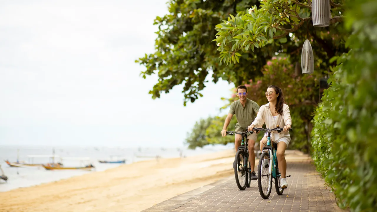 A couple riding bikes along Sanur's sidewalk by the beach