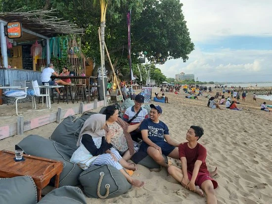 A group of people sitting on the sand and beanbags on Sanur beach